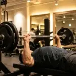 En man i god form utför bänkpress med skivstång på ett modernt gym