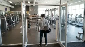 Nybörjare med gymväska står vid entrén och blickar ut över gymmets olika träningszoner
