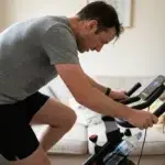 Person mitt i ett spinningpass på en cykel hemma med svett i pannan och vattenflaska på cykeln