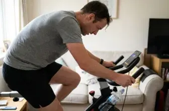 Person mitt i ett spinningpass på en cykel hemma med svett i pannan och vattenflaska på cykeln